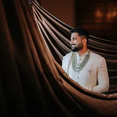 A handsome portrait of the groom in his sherwani, looking thoughtful as he prepares for the ceremony. The dramatic lighting highlights the rich texture of his attire.
