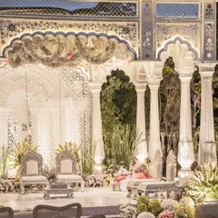 The wedding mandap, a masterpiece of white-on-white elegance. Intricate jali work, Mughal-style arches, and delicate floral garlands create a sacred space that is both grand and deeply personal.