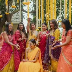 The bride's Haldi ceremony, surrounded by her friends and family. The decor features a canopy of hanging marigold and tuberose strings, creating a traditional and festive ambiance.