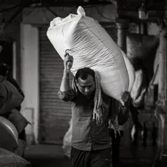 Another worker navigates a narrow, dark alley in the spice market, his determination etched on his face. The single light source creates a powerful, dramatic effect.