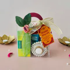 A cute and budget-friendly Diwali gift bag. This transparent bag with a handle holds tea, snacks, and a pearl T-light holder, finished with a "Happy Diwali" tag.