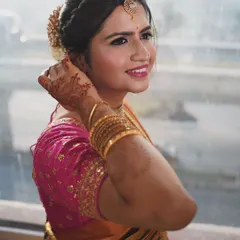 A happy bride glowing on her wedding day. This close-up shows her fresh and radiant makeup, with a bright smile and sparkling eyes. The traditional hairstyle adorned with flowers adds a classic South Indian touch.