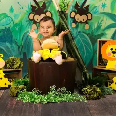 This baby girl is the queen of the jungle, sitting in a wooden bucket with her arms outstretched, surrounded by giraffes and monkeys.