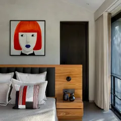 This bedroom in the Mango Orchard House features a bold piece of contemporary art that contrasts with the calm, textured walls and warm wood of the integrated headboard.