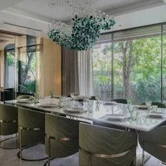 A long shot of the green and gold dining room, showing how it connects to the outdoors through a large window. The long marble table seats ten comfortably, making it ideal for large family gatherings.