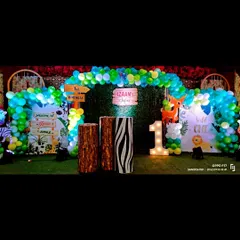 A 'Wild One' first birthday party with a jungle theme. The setup includes a green balloon arch, themed pedestals with animal prints, and a light-up number '1' on a grass-like carpet to complete the safari look.