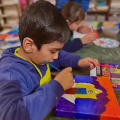 A young student from "Project Mexico" is deeply focused on painting his canvas of a colorful Mexican church.