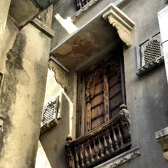 A weathered wooden balcony with detailed carvings, seen in Udaipur. The raw texture of the stone and the aged wood tell a story of time, influencing our use of honest and natural materials.