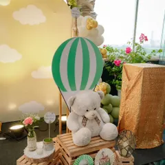 A cozy corner at the travel-themed baby shower. A large teddy bear sits on wooden crates next to a hot air balloon prop, creating a sweet photo opportunity for guests.