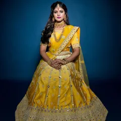A seated portrait showcasing the beautiful drape and detail of the yellow traditional lehenga. The rich color and reflective mirror work ensure you stand out in every photo.