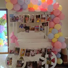 We love adding personal touches to your celebrations. This setup features a charming white cart decorated with a pastel balloon garland and strings of family photos, creating a heartwarming display of memories for a second birthday party.