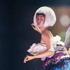 An avant-garde look combining a sculptural dress made from repurposed fabrics with a sharp, white bob wig. This styling choice creates a futuristic and artistic character for a high-concept editorial.