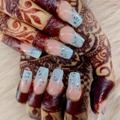 A modern take on bridal nails. These square-shaped extensions feature a soft, natural base with a beautiful baby blue French tip, finished with a sprinkle of delicate silver glitter. This design looks absolutely stunning against the deep color of bridal henna.