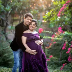 Surrounded by blooming bougainvillea and golden sunlight, this couple shares a warm embrace. A garden setting provides a vibrant and romantic backdrop for a maternity photoshoot.