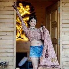 A fun and unconventional bridal portrait. The bride, in her blouse and shorts, joyfully holds up her wedding lehenga, ready for the big day.