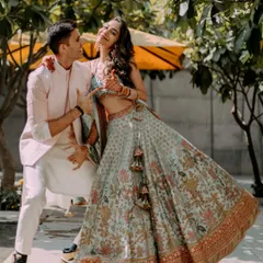 A playful and dynamic shot from a Mehndi ceremony. The couple's fun pose and coordinated pastel outfits capture the happy and relaxed vibe of pre-wedding festivities.