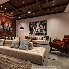 The thoughtful layering of materials, from the warm wood ceiling to the abstract artwork and textured rug, adds depth and character to this comfortable lounge space.