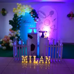 This "Game On" sports theme features a modern arched backdrop with various sports icons. The setup includes custom pedestals and marquee name lighting, perfect for a young athlete's party.