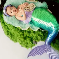A magical mermaid newborn shoot. This tiny baby is dressed in a shimmering mermaid tail, resting peacefully in a giant seashell on a bed of green moss.