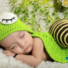 A close-up of the sleeping baby in the green snail costume. The detailed crochet work on the hat and shell adds a special touch to this creative newborn portrait.