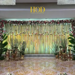 A classic and elegant wedding stage with a backdrop of shimmering gold drapes and a ceiling of hanging floral strings and glass droplets, flanked by traditional brass decor.
