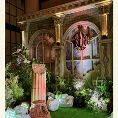 A close-up of the 'ruined garden' mandap. This photo highlights the textural details of the aged-stone-effect backdrop, the overgrown foliage, and the broken columns, all intentionally styled to create a sense of timeless romance.