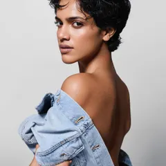 A minimalist and confident shot. The styling is simple, with the denim jacket worn off the shoulder to create a strong line and highlight the model's bare back and sharp haircut.