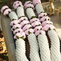 A close up look at the detail and texture of a finished crochet varmala before it gets shipped out. You can see the tightly woven white yarn that forms the base and the individually crafted pink flowers with green leafy accents.