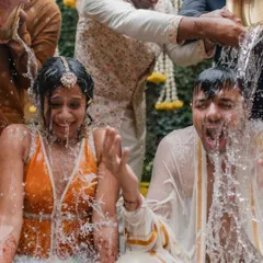 Even a downpour couldn't stop this Haldi. This shot captures the exact moment the couple gets drenched with water, their expressions of shock and laughter showing their amazing spirit.