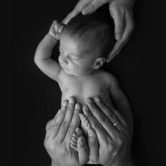A creative and artistic portrait showing a newborn held within a frame of their parents' hands. This black and white shot emphasizes how small and precious they are.