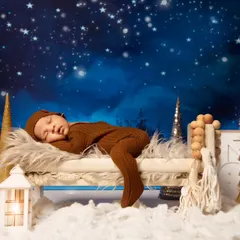 This little one is stretched out and sleeping on a miniature wooden bed, surrounded by a wintery, star-lit forest scene. It’s a perfect example of a cozy and imaginative newborn portrait.