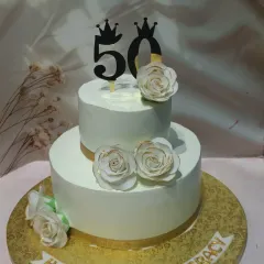A clean and classic two-tiered cake for a 50th birthday. The design is simple and elegant, with white sugar roses and a gold ribbon accent, letting the milestone speak for itself.
