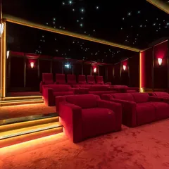 A magnificent red-themed cinema room featuring a combination of plush sofas and tiered seating. The design is elevated by a full starlight ceiling and warm, indirect lighting along the steps and walls, creating a truly luxurious viewing environment.