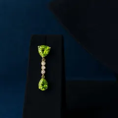 A closer look at our peridot and diamond pendant. The trillion-cut stone at the top, the line of brilliant diamonds, and the pear-shaped drop are all set in warm gold to create a piece fit for queens, worn your way.