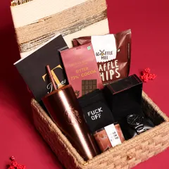 A luxury Christmas hamper for him, packed in a rustic jute-woven box. It includes a Starbucks-style tumbler, a watch, a cold brew coffee candle, and gourmet chocolates.
