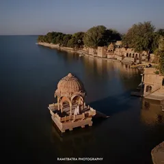 A breathtaking aerial shot of a couple standing in a cenotaph seemingly floating on Gadisar Lake in Jaisalmer, a truly magical pre-wedding moment.
