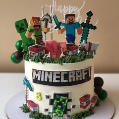 A fun Minecraft cake featuring Steve, a Creeper, and TNT blocks. The design includes a pixelated border and grassy buttercream top.