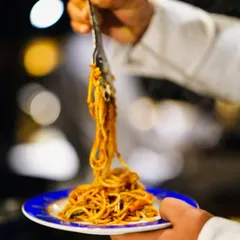 A chef plating a fresh serving of spaghetti at a live pasta station. This action shot captures the process of creating customized pasta dishes for guests, ensuring every plate is hot and delicious.