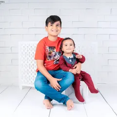 A heartwarming portrait of two brothers. The older brother smiles proudly while holding his baby brother, showcasing their special bond.