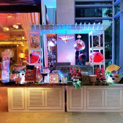 A Pan-Asian themed food station with a white slatted counter and decorative elements like Japanese fans and disco balls. This setup for a corporate event at Hotel Andaz shows our ability to create visually engaging and thematic culinary displays.
