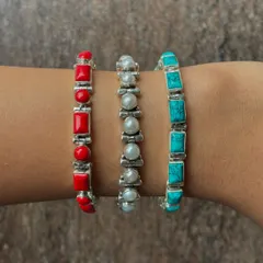 A stack of three of our popular stone bracelets. This image showcases the vibrant red coral, classic white pearl, and serene blue turquoise options, all set in sterling silver.