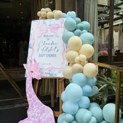 A personalized welcome sign for Chandni and Akshit's baby shower. The entrance is decorated with a pastel balloon garland and a pink giraffe cutout, setting a sweet and inviting tone.