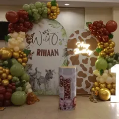 A "Wild One" safari theme for Riaan's first birthday. This setup features two custom backdrops, one with animal prints and another with jungle illustrations, surrounded by a balloon garland in olive green, gold, and brown.