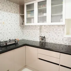 A wider view of the kitchen with the 3D geometric backsplash, paired with off-white lower cabinets and a black granite countertop. The design is minimalist yet full of interesting details.