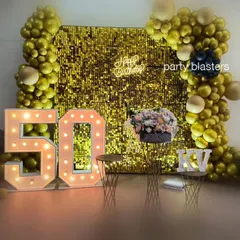 A stylish 50th birthday photo corner. The shimmering gold sequin wall, marquee numbers, and elegant floral arrangement create a perfect spot for memorable pictures.