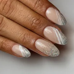 Go all glittery with this dazzling design. It features a cascade of silver glitter over a nude base, with abstract white spider gel lines for a modern, artistic touch.