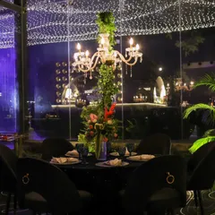 An elegant table setting inside a glass-walled section of the venue. The design allows guests to feel connected to the outdoor ambiance while enjoying the comfort of an indoor setting, all under a canopy of fairy lights.