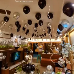 An immersive party atmosphere created with black and silver helium balloons covering the ceiling of a cafe or large living room.