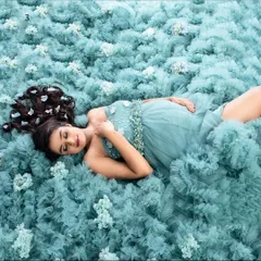 A dreamy, ethereal portrait created by having the client lie on a bed of soft, ruffled teal fabric. This overhead shot, adorned with small flowers, creates a unique and artistic 'sleeping beauty' effect.
