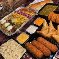 A close-up of the delicious components of my Iftar box. You can see the rich biryani, crispy samosas, savory rolls, and creamy curries, all packed neatly and ready for your celebration.
